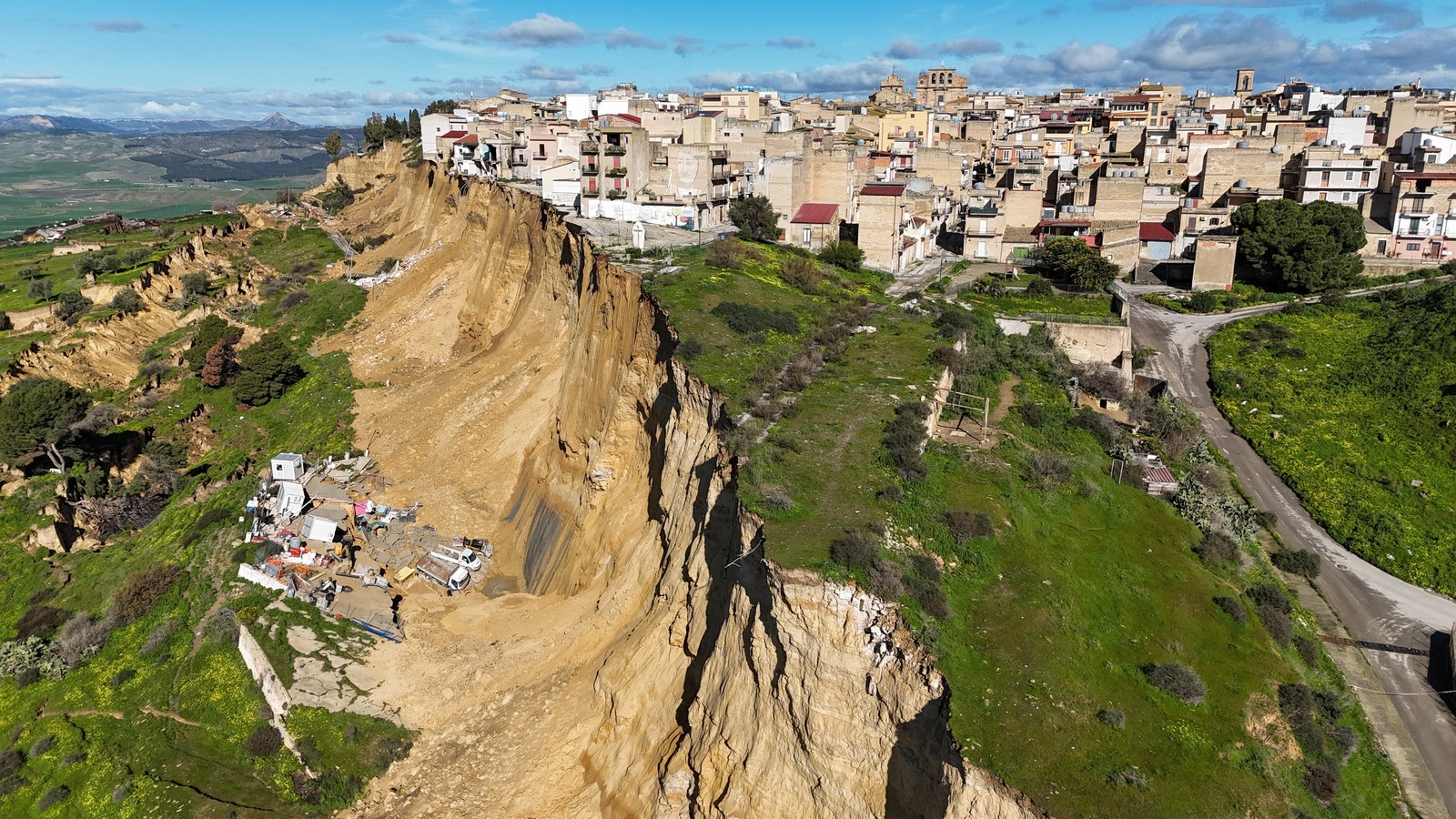 An aerial view shows houses perched along the edge of a cliff after a landslide.
