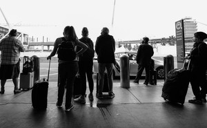 A black and white photo of travelers with suitcases wearing masks