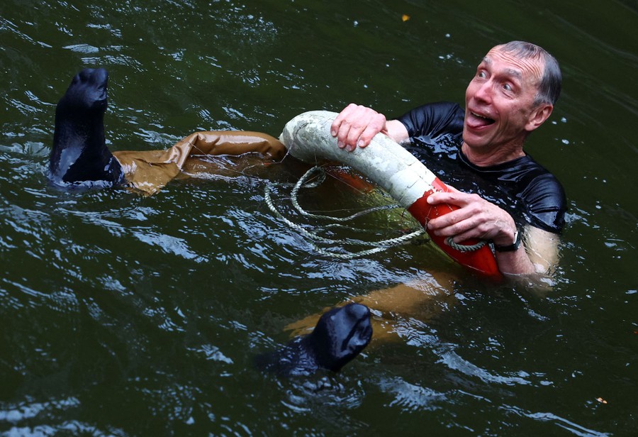 A man makes a playful face while floating, fully clothed, in a pond.