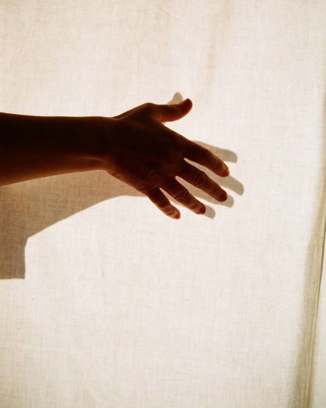 a hand outstretched in front of a white curtain, its shadow beneath it