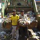 Garbage collectors in Bangalore stand in front of a garbage truck. One holds a basket of trash.