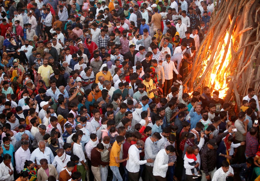Dozens of people gather closely together around a large bonfire.