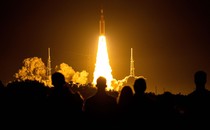 People watch as a large rocket blasts off at night.