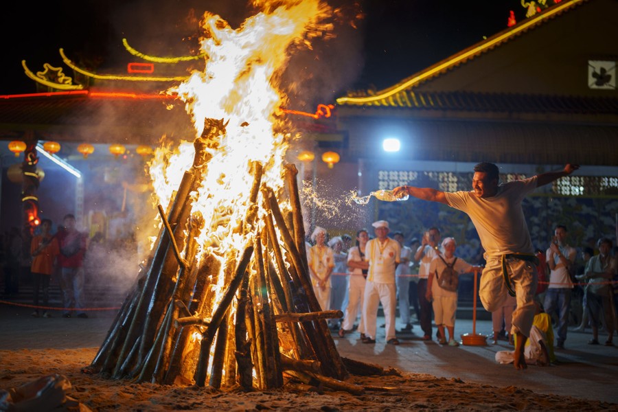 A man tosses fuel on a bonfire.