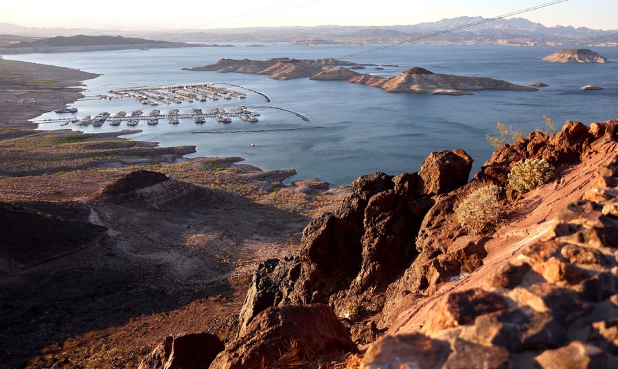 A broad view from a hilltop of Lake Mead, a floating marina, and surrounding hills.