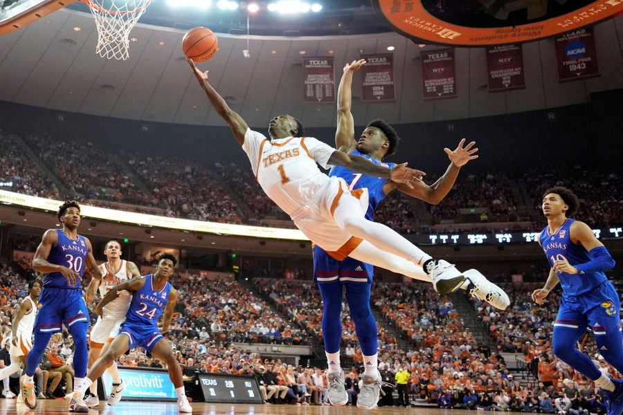 A basketball player leaps and reaches for the basket during a game in a stadium.