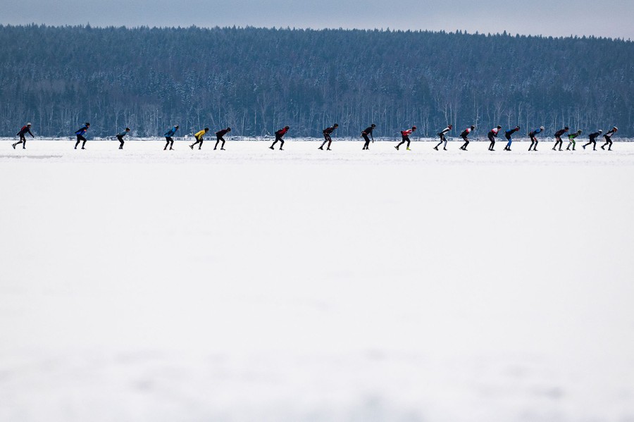 A line of a couple dozen skaters is seen on a frozen lake.