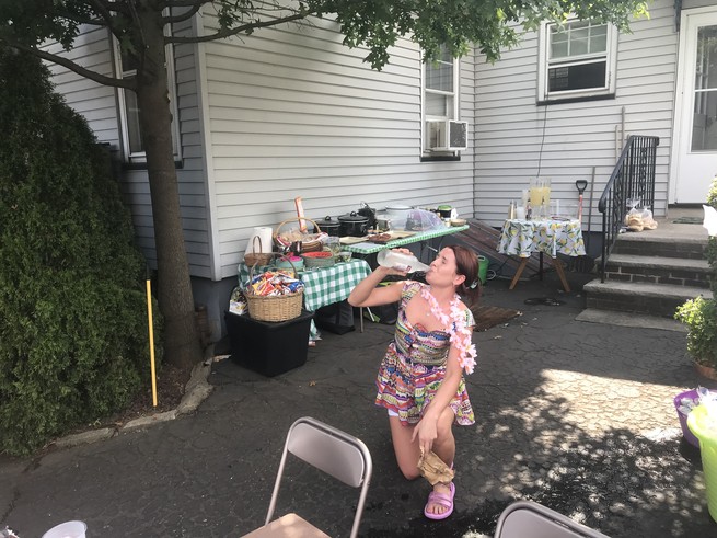 A woman kneeling in a driveway, drinking a Smirnoff Ice.