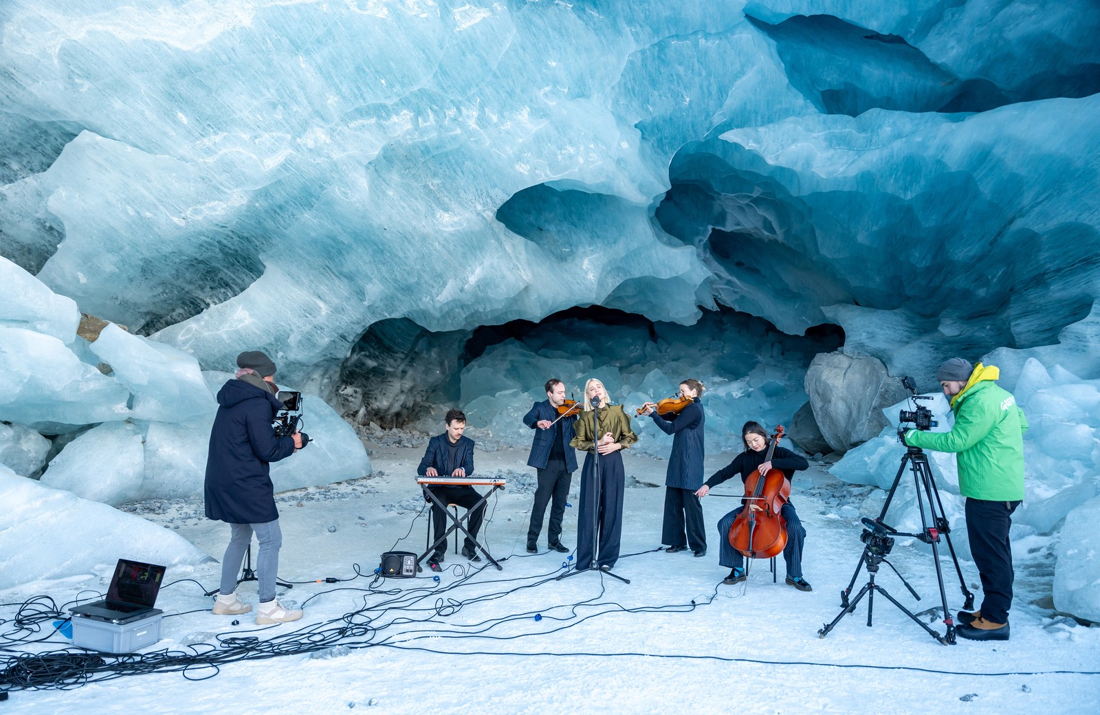 A group of musicians performs beside a glacial cave.