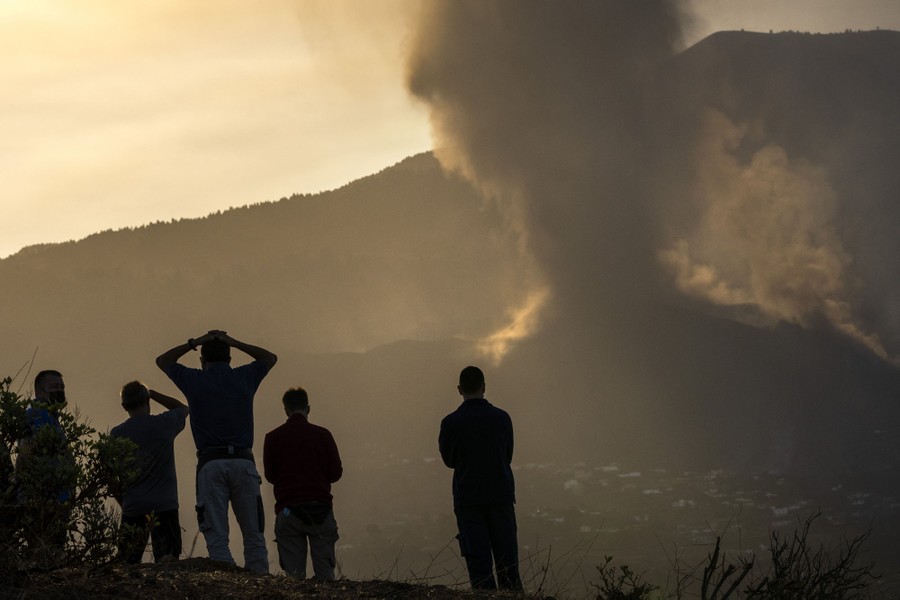 Several people stand together watching a an eruption on a distant slope.