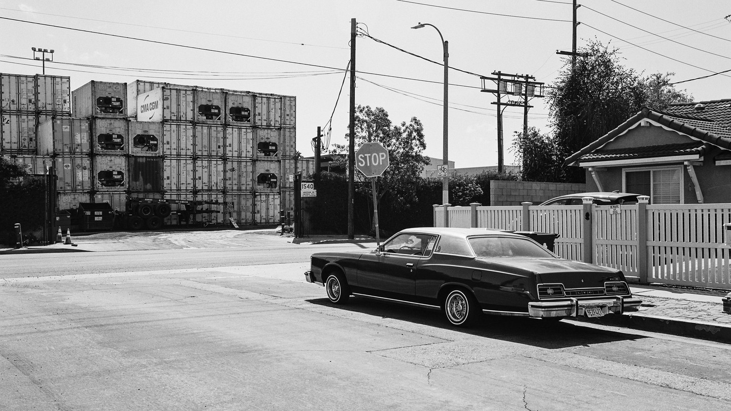Black-and-white photo of a car at a stop sign and shipping containers across the street
