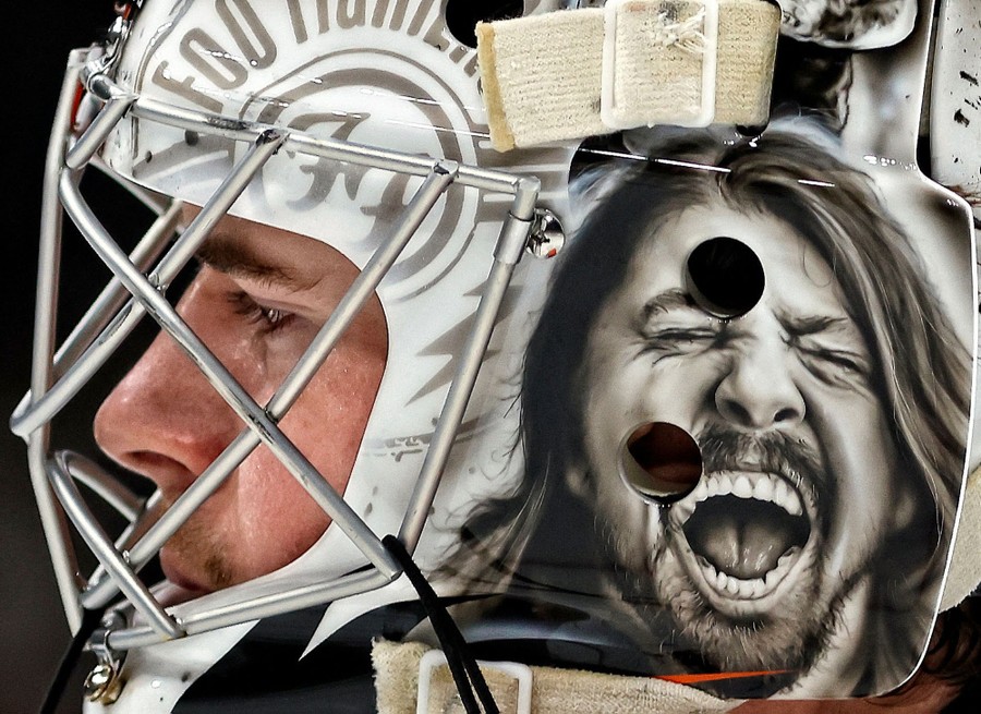 A hockey player wears a large mask with the face of performer Dave Grohl painted on it.