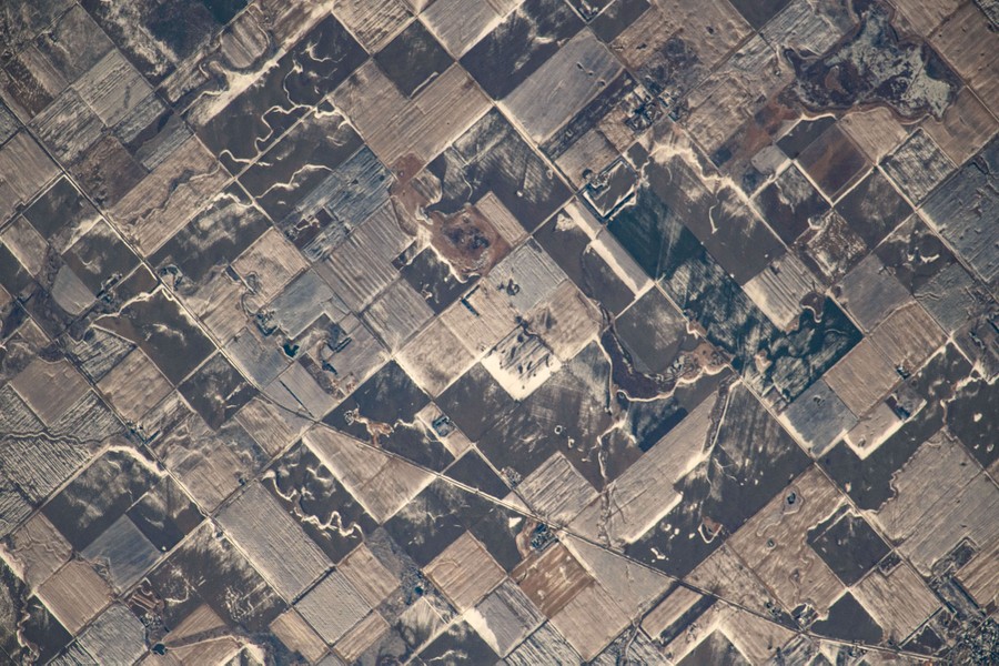 An elevated view of many square farm fields dusted with snow.