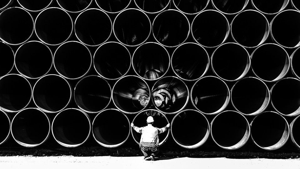 Large pipes for the Baltic Sea pipeline Nord Stream 2 are stacked in a storage area in the ferry port of Sassnitz/Neu Mukran. An employee of the responsible company Wasco crouches in front of the pipes.