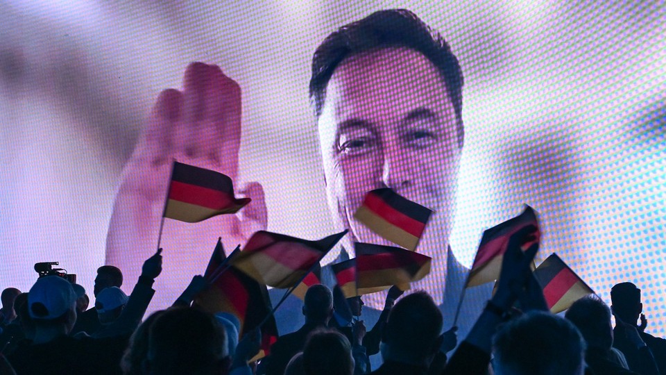 Photo of a crowd holding German flags watching a screen with Elon Musk waving