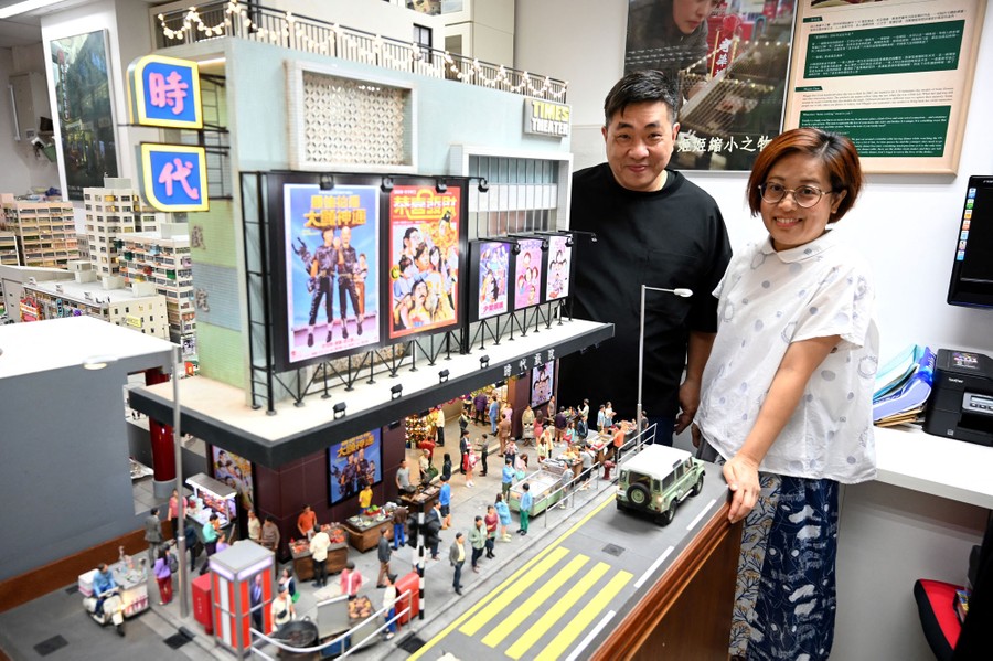 Two model makers pose beside one of their scale models of a building and sidewalk.