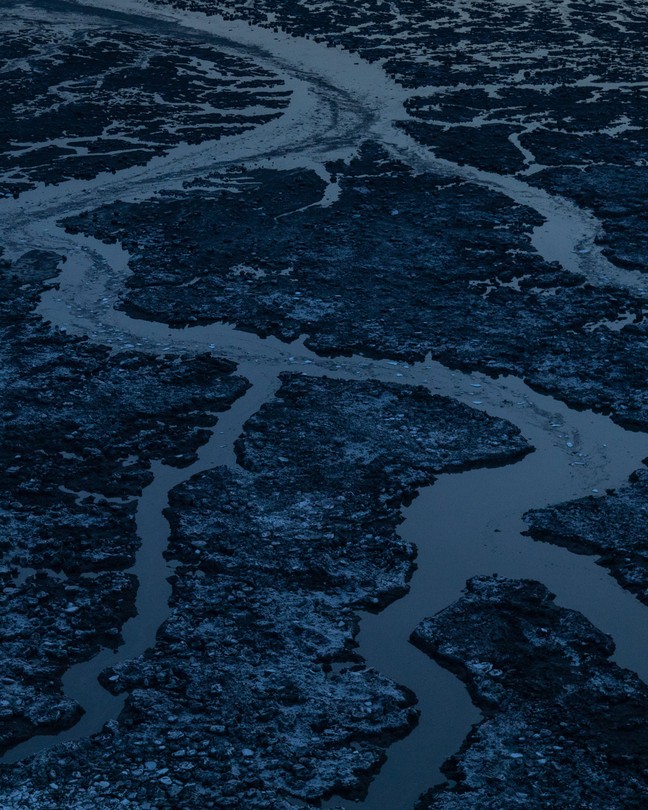 Ice masses break up a body of water in a dark landscape.