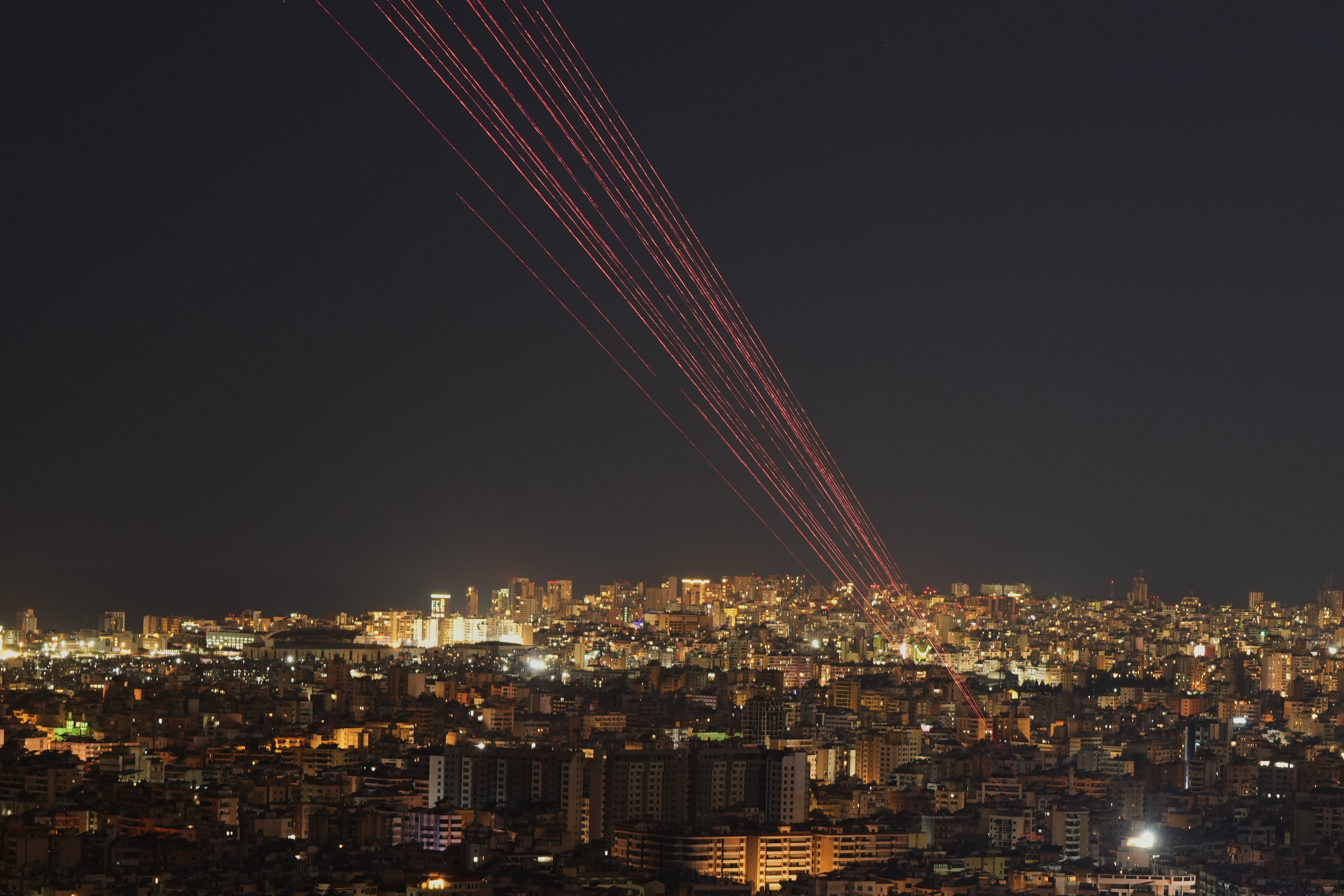 Streaks of light from tracer rounds fired into the sky, seen above a city at night.