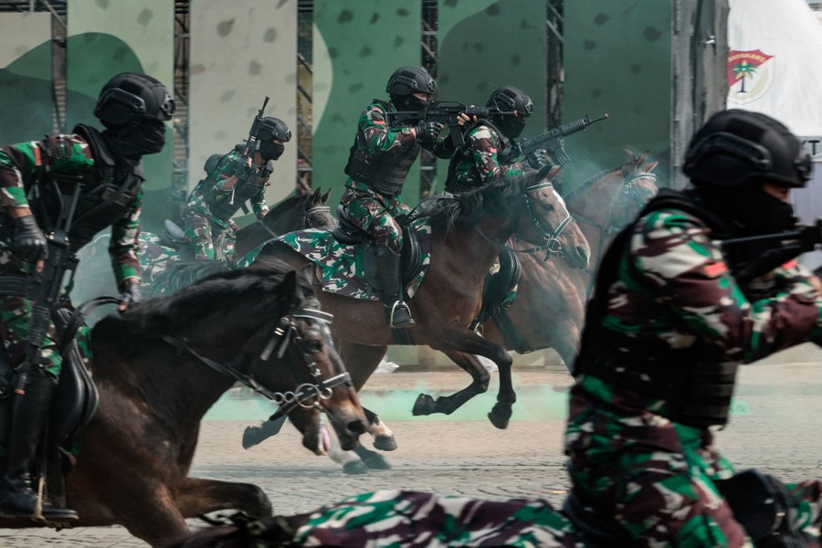 Several soldiers in riot gear ride horses at a gallop.