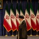 Khamenei, looking down, walks past a bank of seven Iranian flags with a portrait of Ayatollah Ruhollah Khomeini above them.