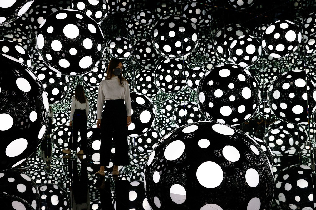 A person stands among illuminated spheres in a mirror-walled room.