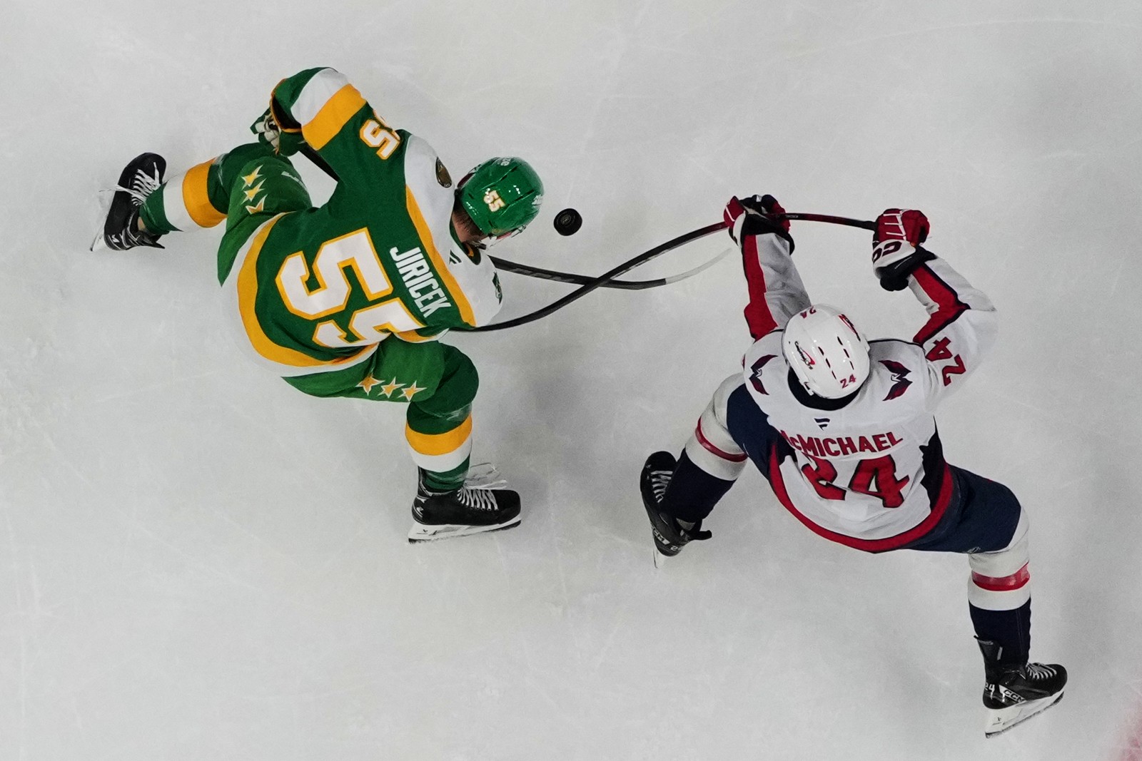 Two hockey players cross sticks, vying for a puck.