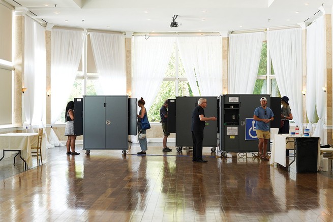 photo of high-ceilinged room with large windows and wood floors being used as voting center with booths and tables