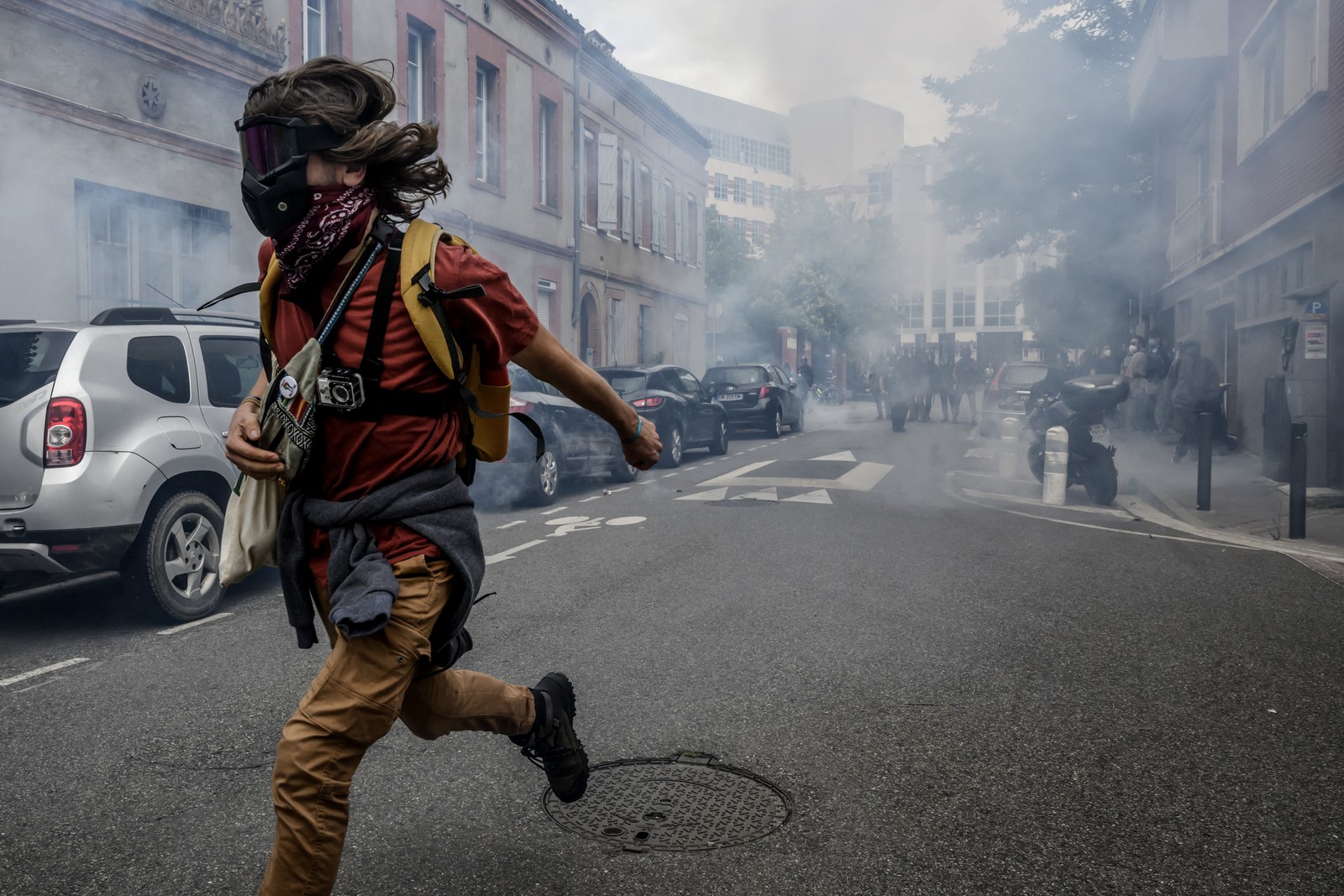 A masked protester runs on a street, fleeing from riot police.