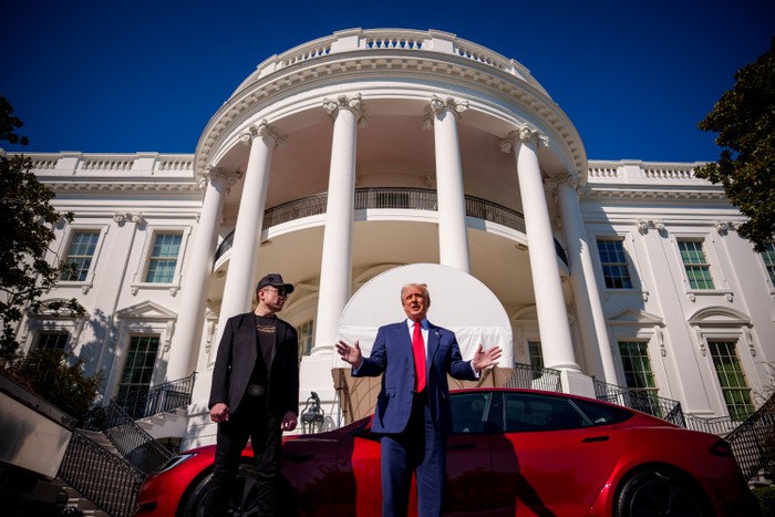 Elon Musk and Donald Trump stand in front of a red Tesla that's parked in front of the White House