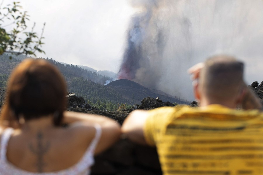 People watch as a volcano erupts in the distance.