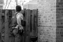 An armed Homeland Security officer peers over a wooden fence