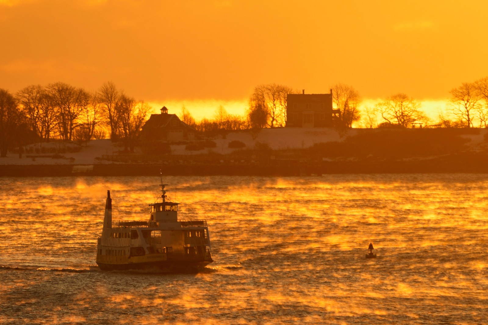 Patchy fog rises from the water of a harbor as a ferry passes by at sunrise.