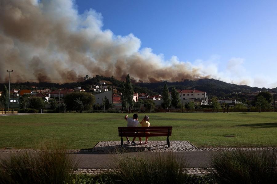Two people sit on a park bench looking at smoke from a nearby wildfire.