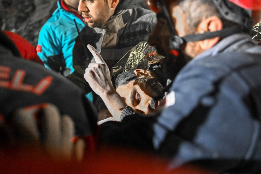 A man holds up one finger as he is carried by rescue workers.