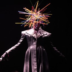 Grace Jones performs onstage wearing a head covering made of many colorful sticks.
