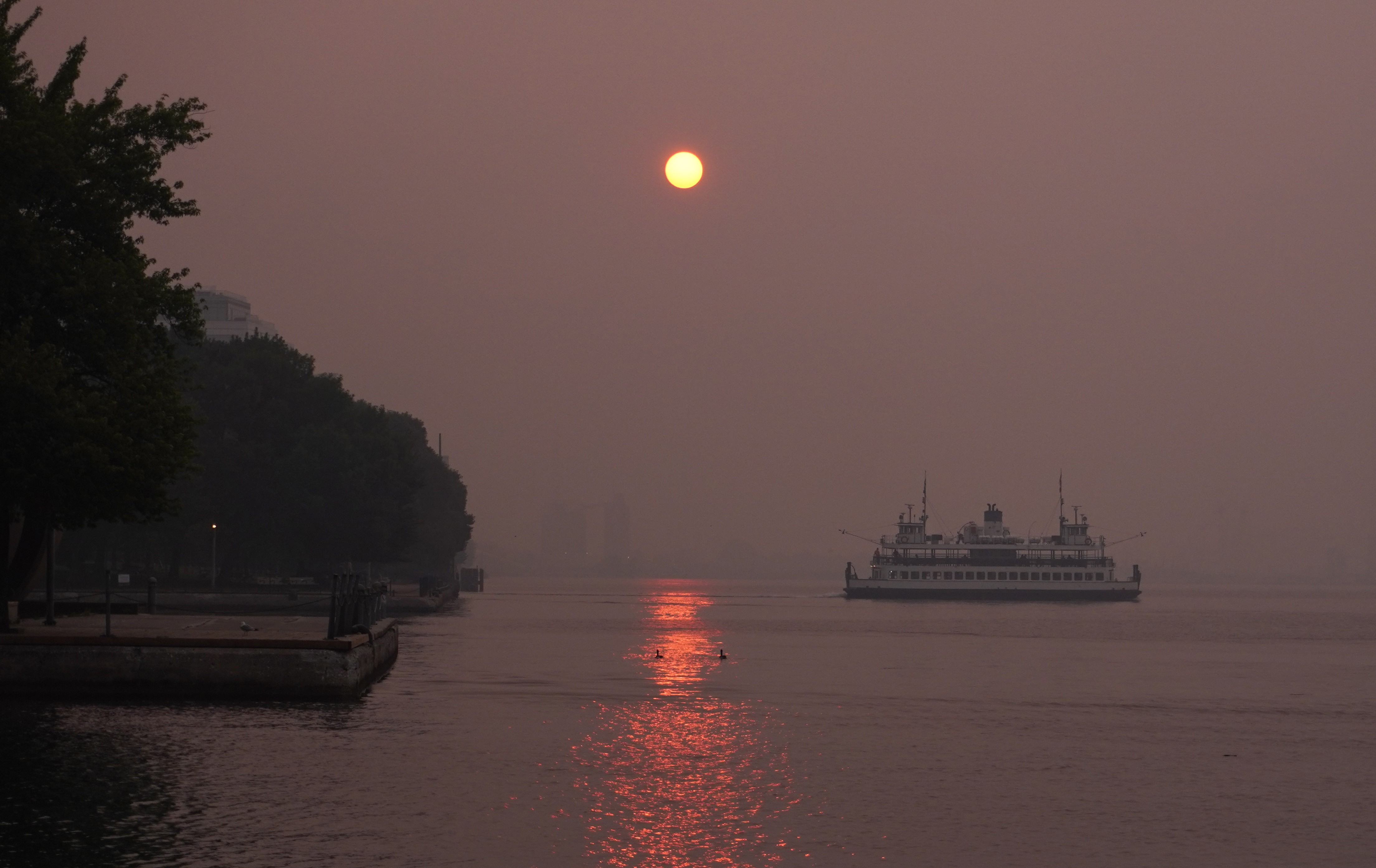 The sun rises over a waterfront on a smoky day, as a ferry passes by.