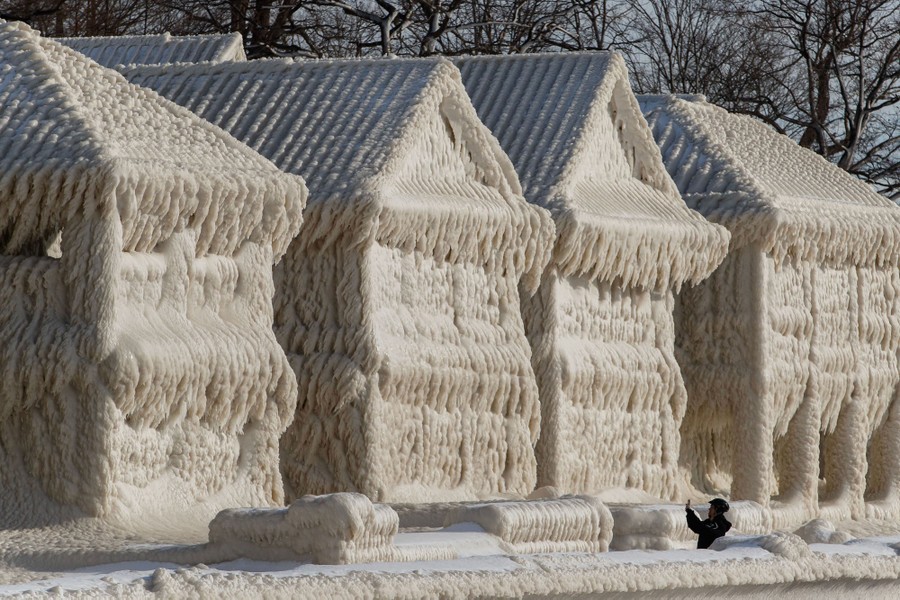 A person photographs several houses that are completely encased in ice and icicles.