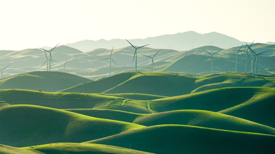 Wind turbines spin over a Elysian landscape of green fields