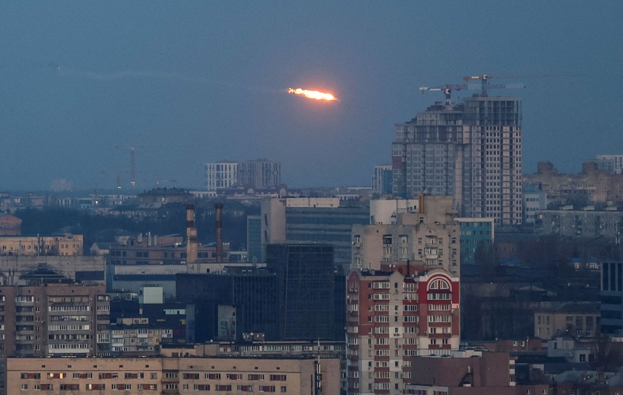 A fireball streaks through the sky above the buildings of a city during a missile and drone strike.