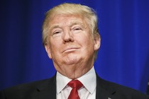 Trump in suit smirks beside an American flag