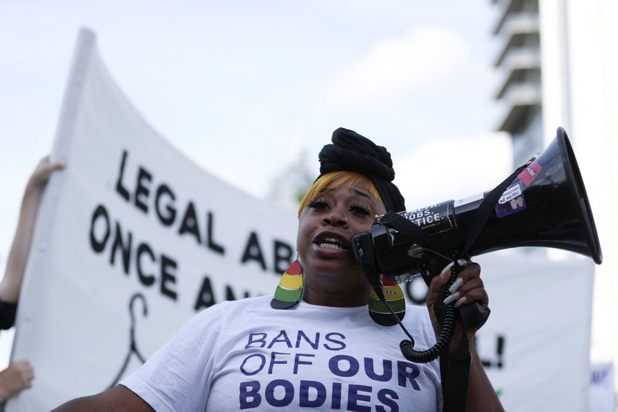 A person wearing a T-shirt that says "bans off our bodies" speaks into a megaphone.