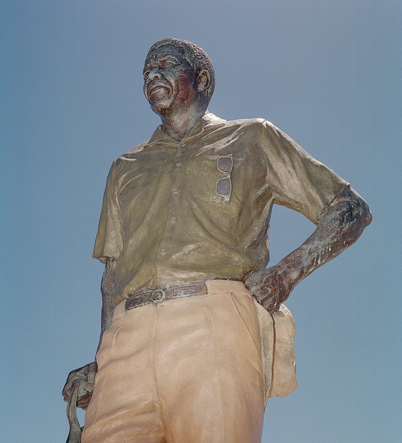 photo looking up at statue of Mandela with one hand leaning on shovel and the other hand on his hip