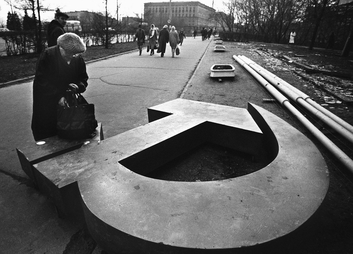 امرأةٌ تمدّ يدها في حقيبتها، الّتي وضعتها على شعار مطرقةٍ ومنجلٍ سوفيتّيٍّ سقط في أحد شوارع موسكو عام 1991.
