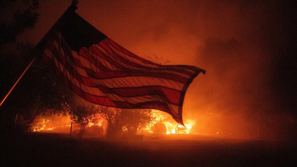 An American flag waves in front of a wildfire.