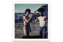 A polaroid of two people facing the camera, wearing casual clothing and afros, with their palms clasped together.