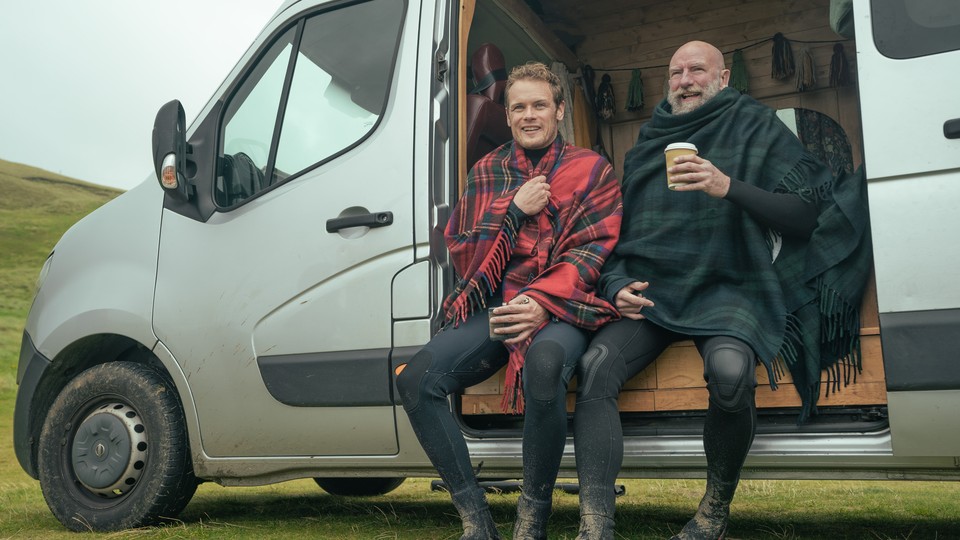 Two men in kilts sit in the open door of a van
