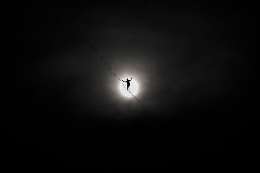 A tightrope walker high in the distance, silhouetted by the sun