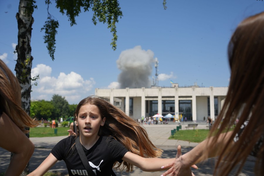 Several people run from a public square, with a rising cloud of smoke visible behind a nearby building.