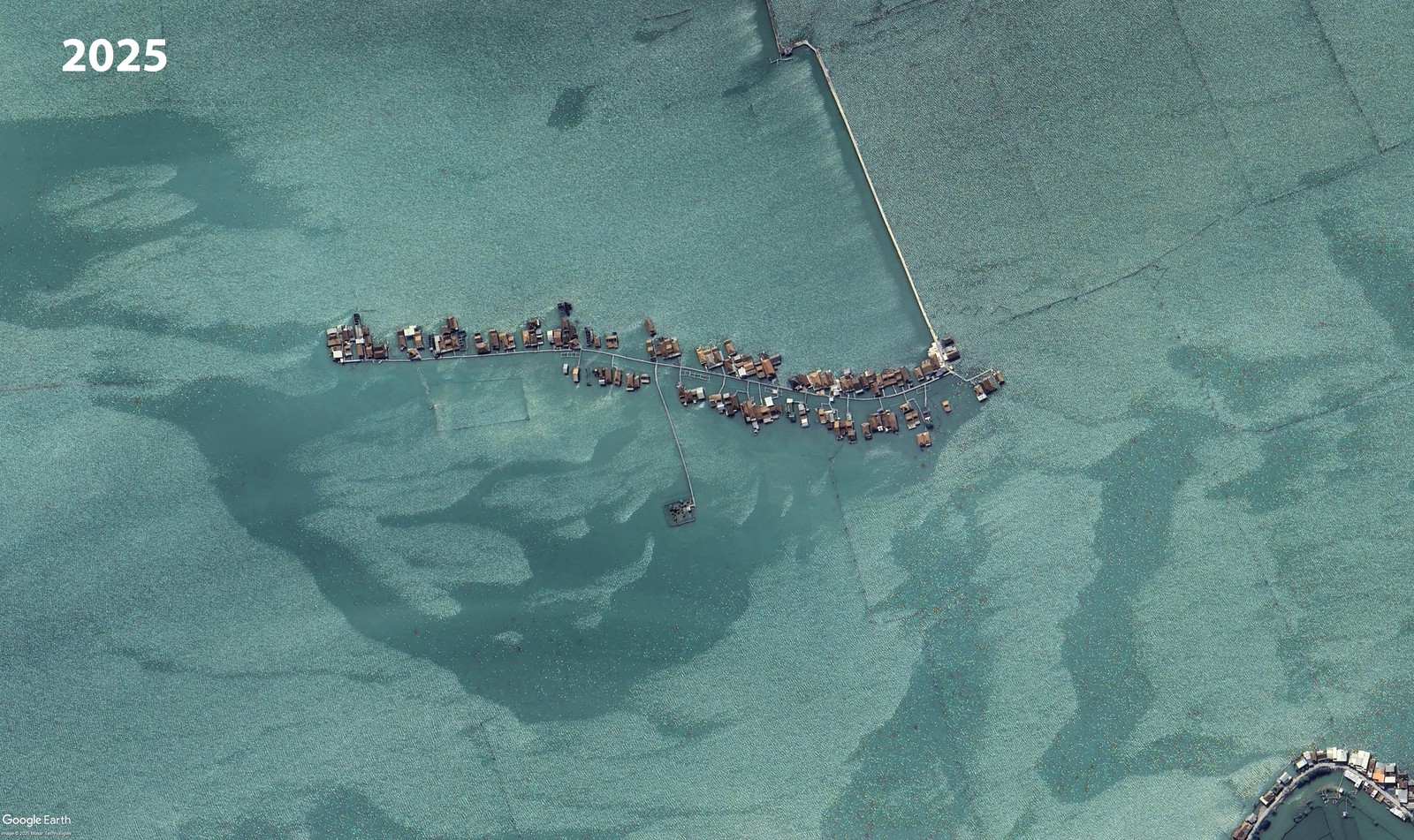 A satellite view showing the same cluster of houses from the previous photo, surrounded by shallow seawater