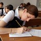 Students in uniform take an exam in a classroom using pencil and paper.